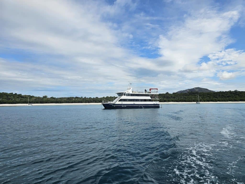 Passenger ferry on calm water with a forested shoreline and blue sky streaked with clouds.