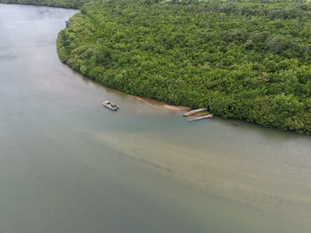 Aerial view of a mangrove-lined riverbank with a small boat near a sandy shore.